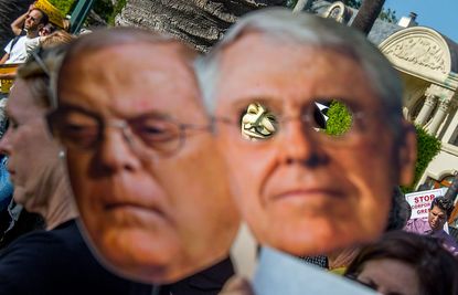 Protesters hold up masks of David and Bill Koch