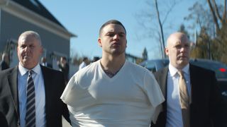 Patriots&#039; tight end Aaron Hernandez (Josh Andrés Rivera) being led away by two police officers in American Sports Story season 1