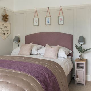 White bedroom with upholstered headboard, wall lights, wall panelling and wall hanging