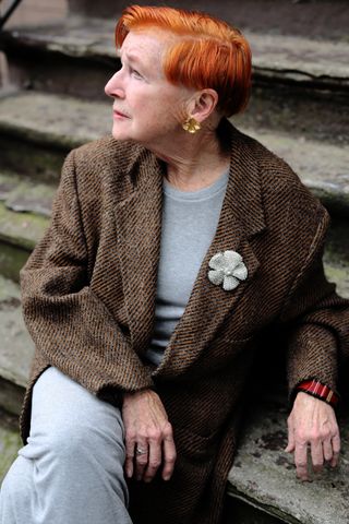 A photo of Alice Carey in an over 60 outfit featuring a gray dress, brown tweed blazer, silver brooch, and gold earrings.