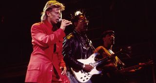 David Bowie wears a red suit as he performs onstage at Giants Stadium with Carlos Alomar on guitar, Carmine Rojas on bass.