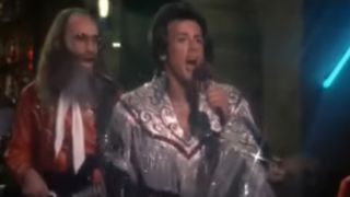 Sylvester Stallone singing on a stage in a glittery, frilly top