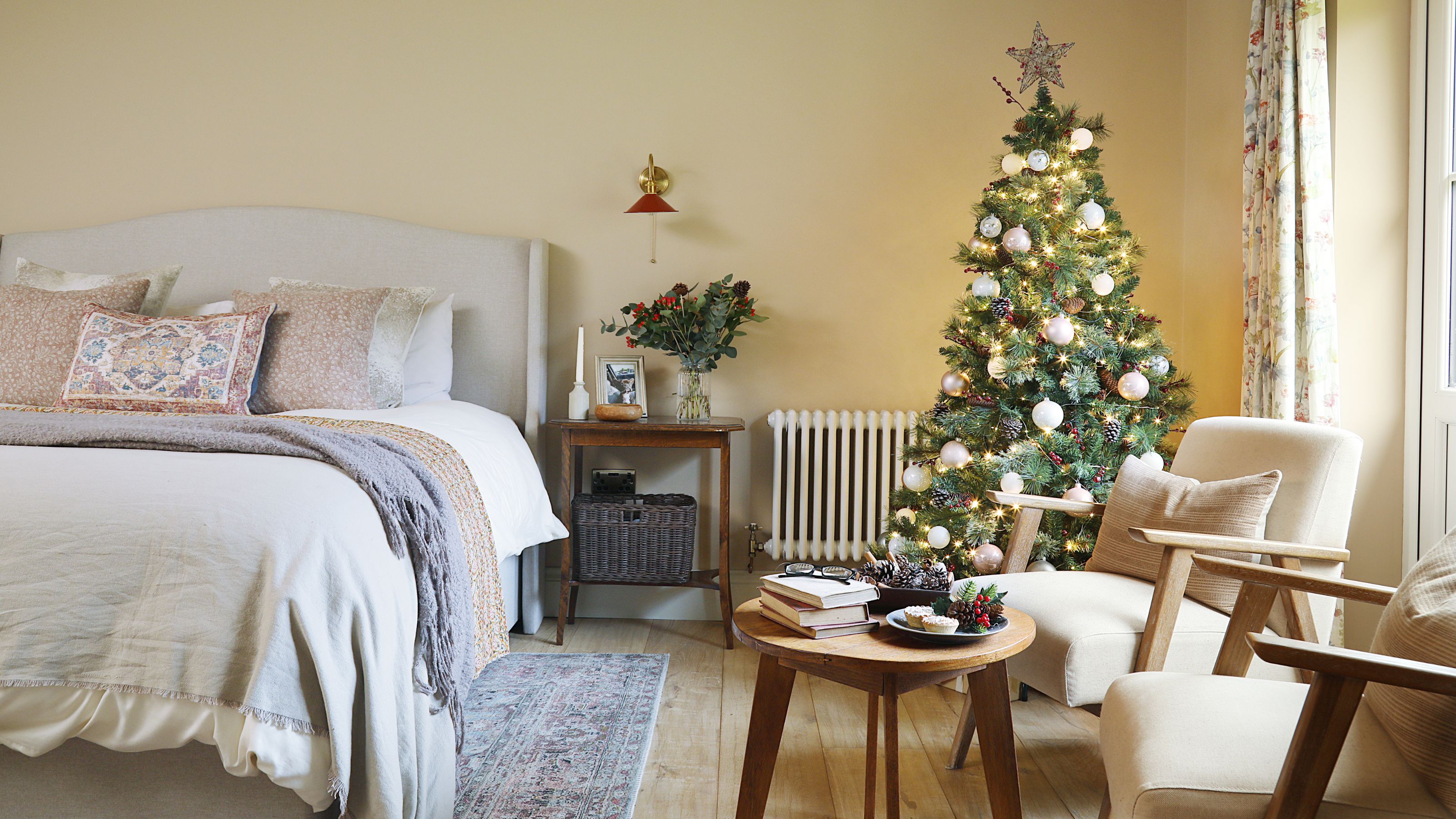 Bedroom with a bed on the left, two chairs and a coffee table on the right, and a christmas tree behind it