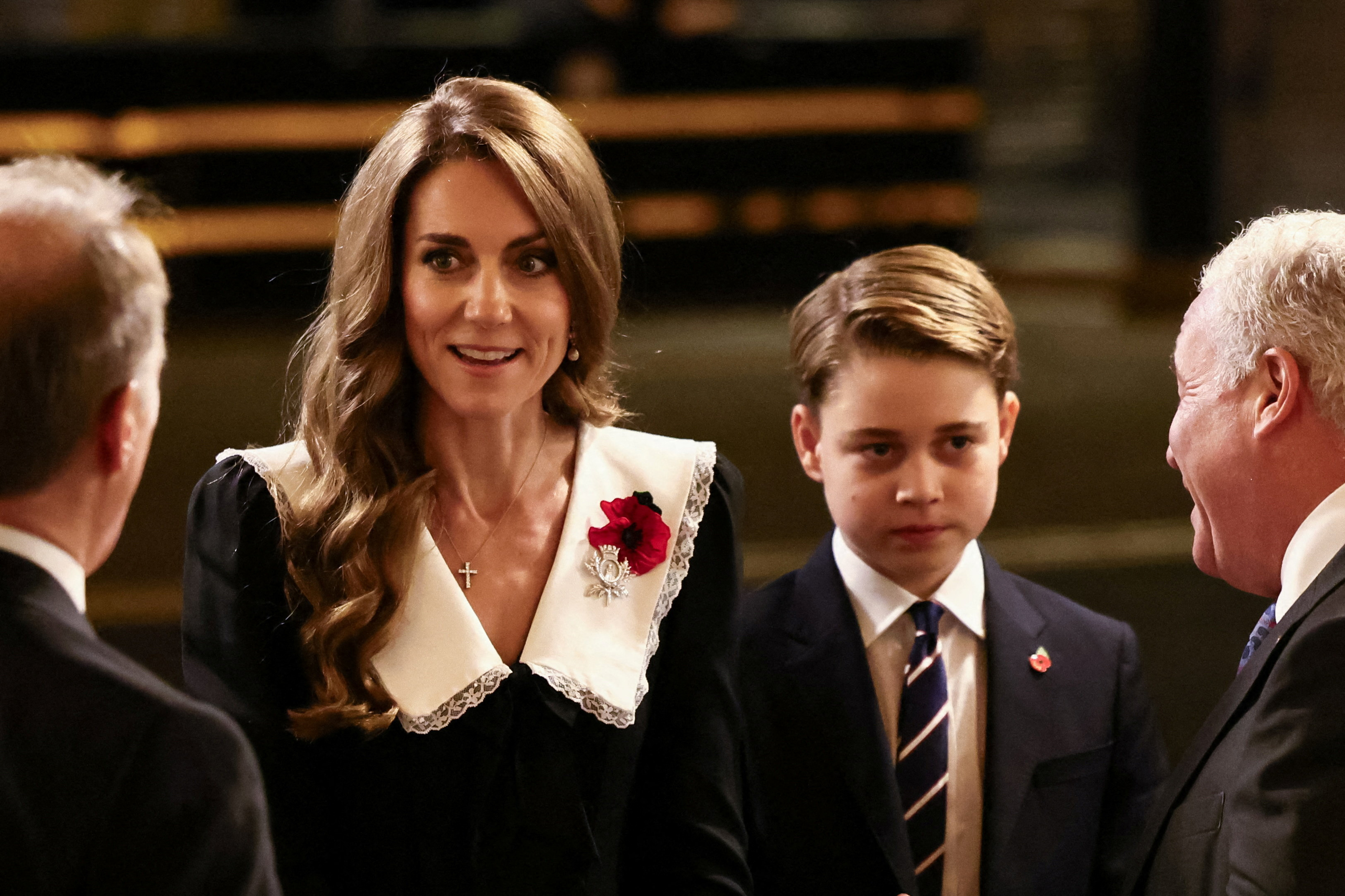 Princess Kate wearing a dress with a white collar standing next to Prince George, in a suit