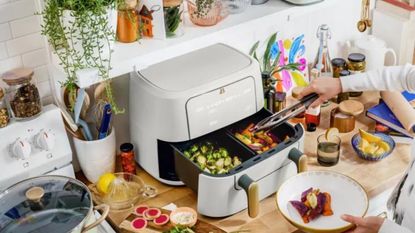 Drew Barrymore beautiful 2-drawer air fryer in white icing colorway on busy kitchen countertop