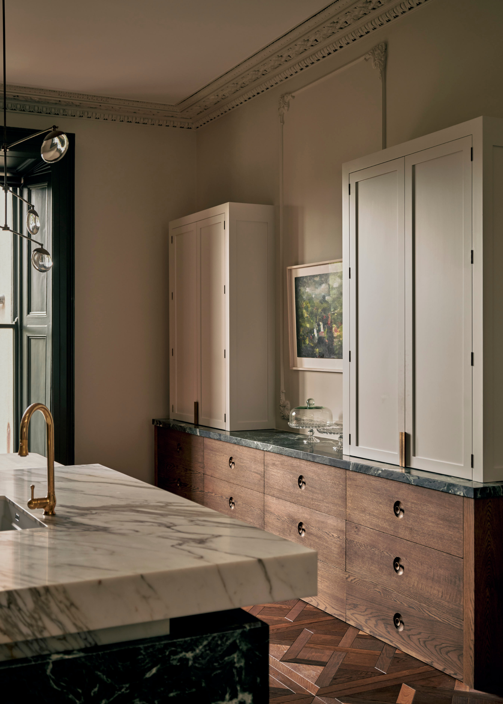 A kitchen with white cupboards, stone marble counter, and wood drawers by a white and black stone kitchen island with a gold tap