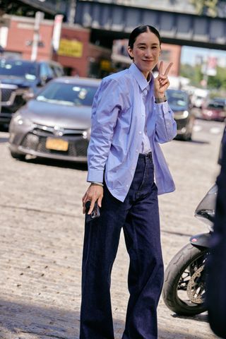 Eva Chen wearing dark-wash high-rise wide-leg jeans, a white tee shirt, and a blue button-down shirt standing in the street at New York Fashion Week