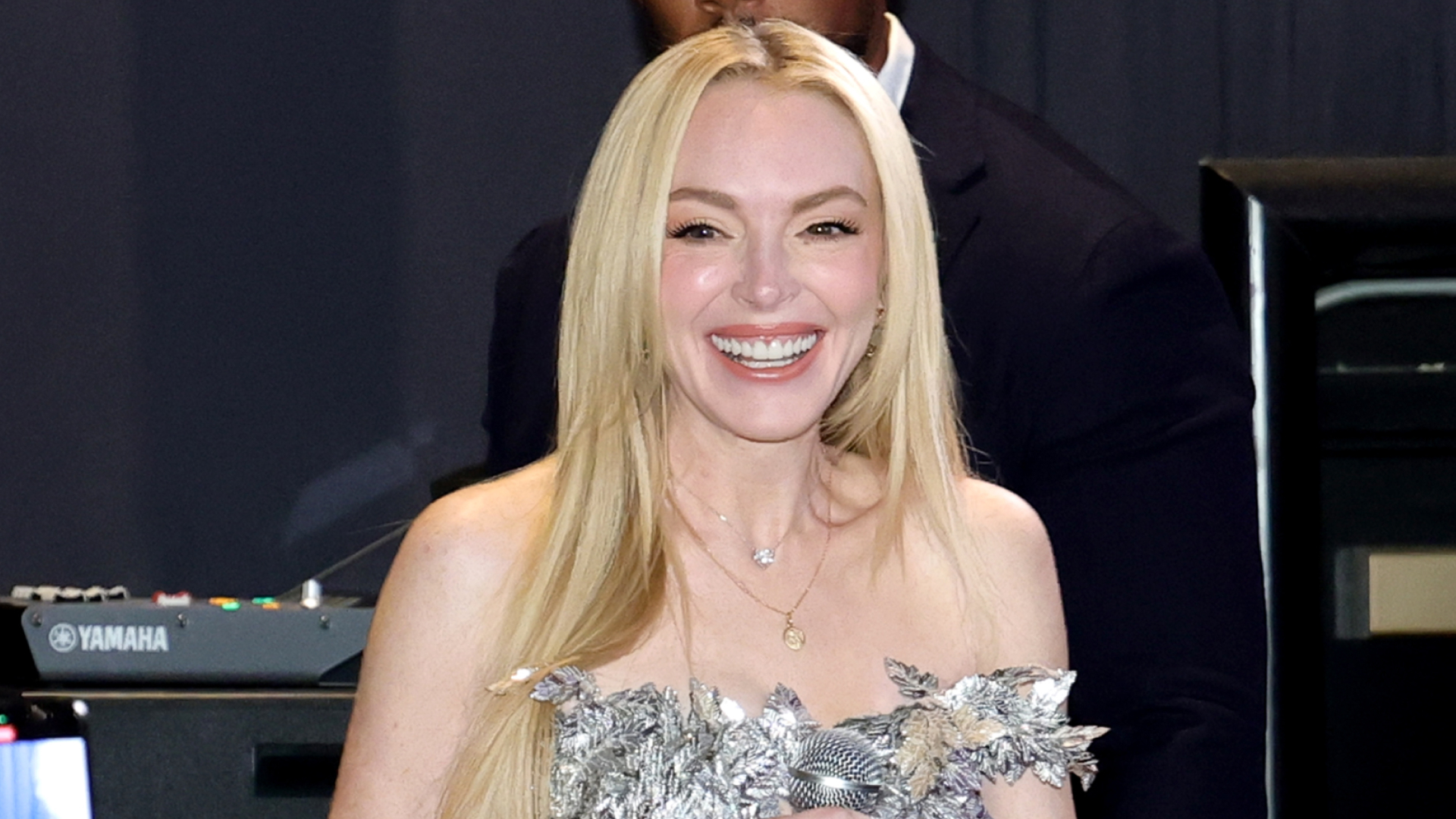 Lindsay Lohan wears a metallic strapless top, white pants, a Cartier watch, and carries an Hermes Kelly bag