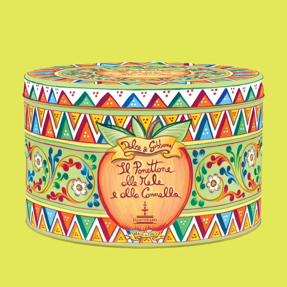 An intricately decorated panettone tin box with bright floral motifs in green, red, blue, yellow, and orange, with an apple-shaped drawing both on its lid top and on either end of its sides.