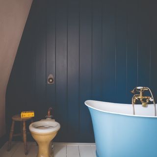 A bathroom with a sky blue bath tub and a panelled wall painted in Farrow & Ball's Hague Blue shade