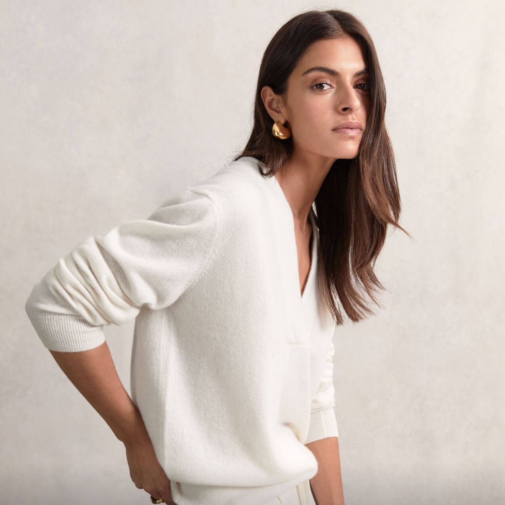 Young brunette woman wearing white sweatshirt and gold earrings, looking at camera.