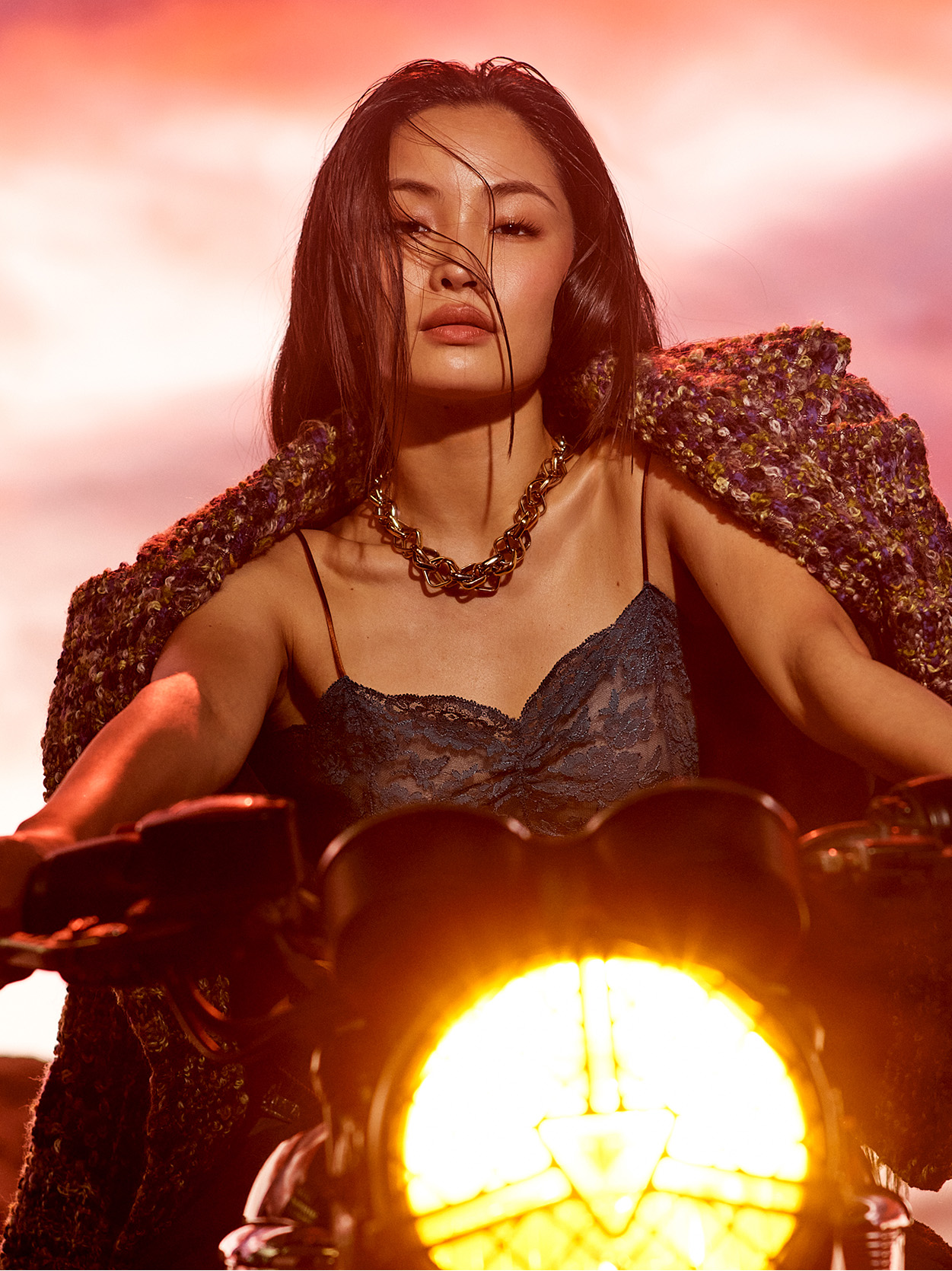 Anna Sawai sits on a motorcycle wearing a lace camisole and textured jacket.