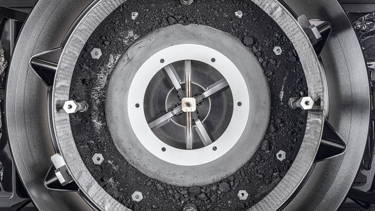 A top-down view of the OSIRIS-REx Touch-and-Go-Sample-Acquisition-Mechanism (TAGSAM) head with the lid removed, revealing the remainder of the asteroid sample inside.