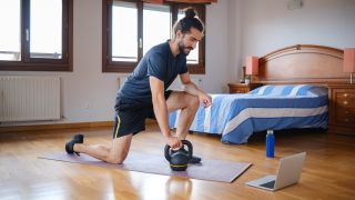 Man kneels holding kettlebell at home