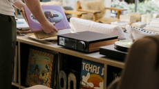 A photo of the Cambridge Audio Evo 150 SE atop a unit packed with vinyl records. A person is to the left of the amplifier looking at record sleeves but most of the person is cropped out