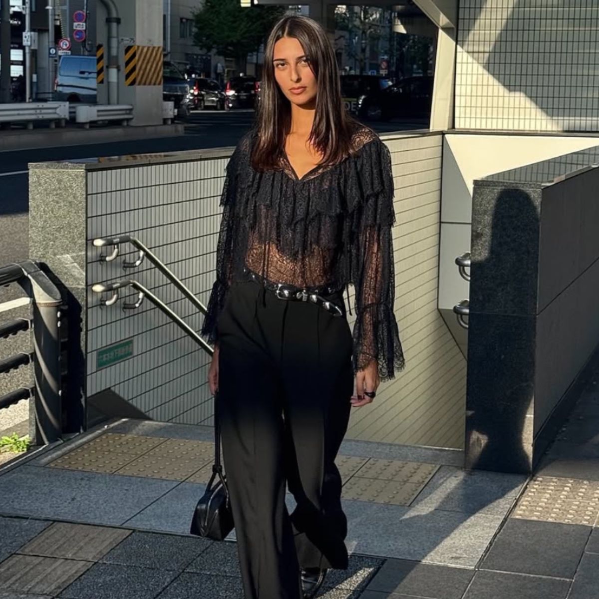 A woman wears black pants with a black lace shirt 