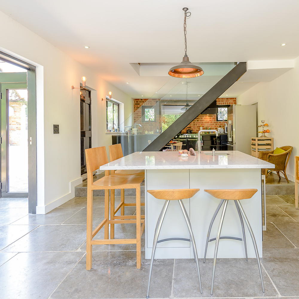 Modern kitchen with island and chairs with brass hanging light and staircase