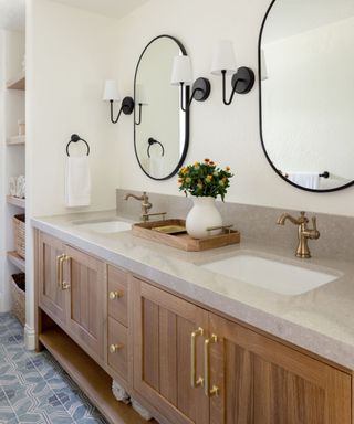 California casual style bathroom with wooden cabinets, a marble counter, gold hardware and black metal accents