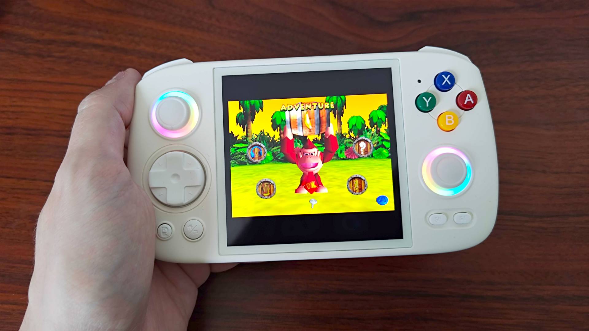 Hand holding Anbernic RG Cube with Donkey Kong 64 main menu on screen.