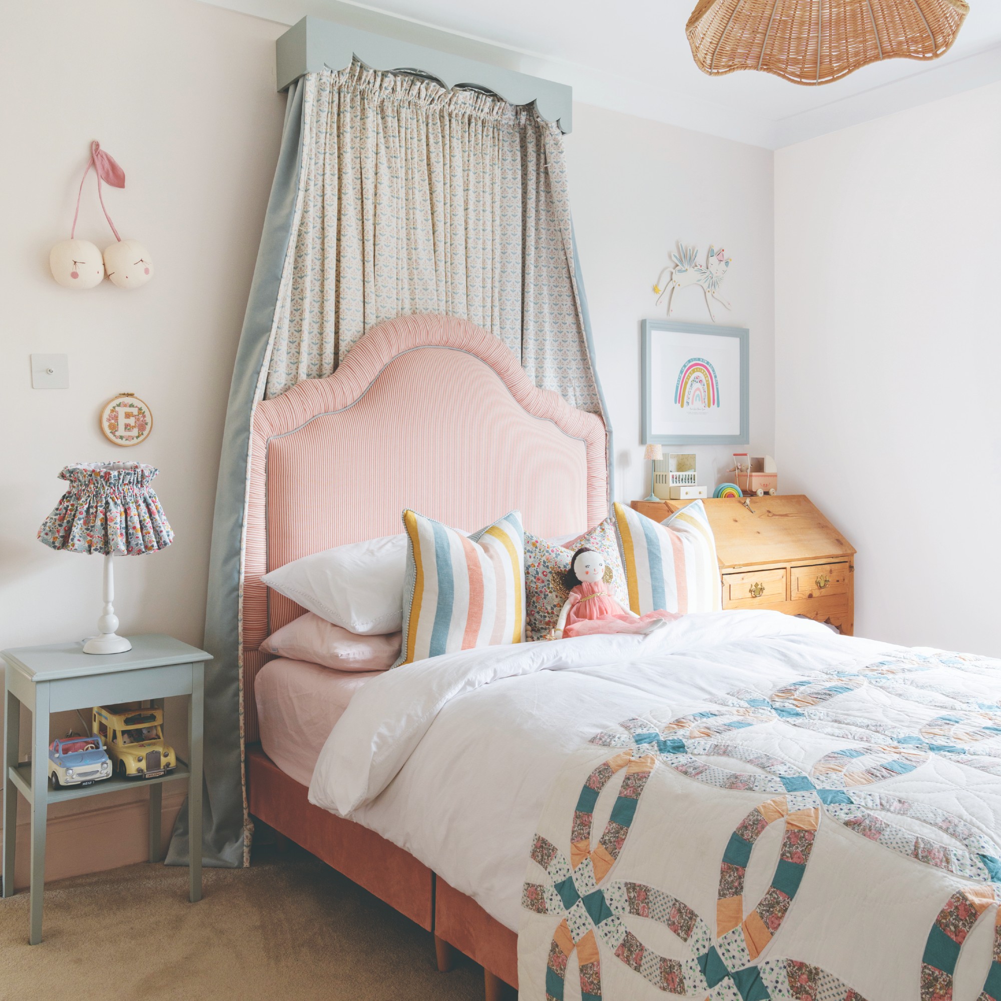 A child's bedroom with a pink upholstered bed headboard and a pastel green canopy