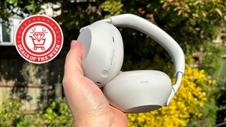 Sony WH-1000XM6 headphones being held in one hand in a garden with a Deals of the Week logo alongside