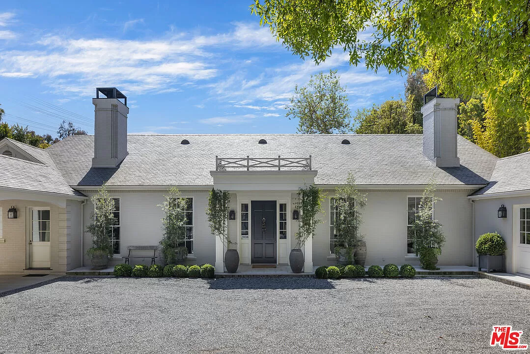 The front of a symmetrical single story home painted light grey with potted plants outside