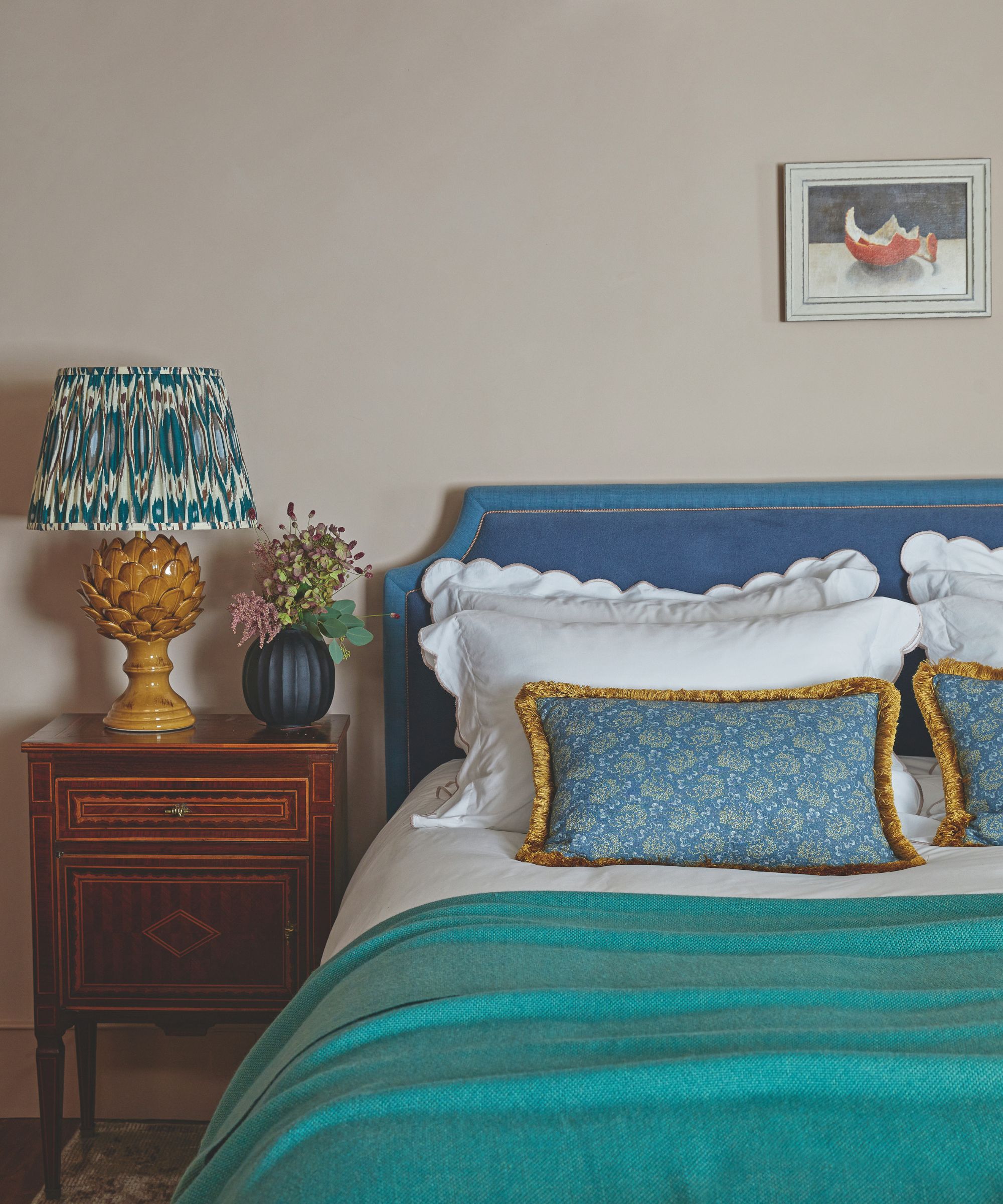 Bedroom with warm beige walls and bed with blue headboard and turquoise throw with a wooden bedside table