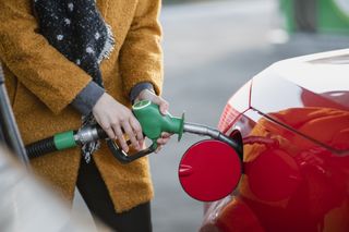 Close up of a woman filling up a red car with petrol at a petrol station