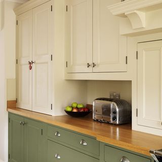 cream kitchen with soft green painted cupboards, wooden floors and countertops