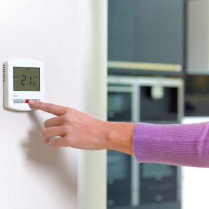 Hand adjusting a digital thermostat on the wall