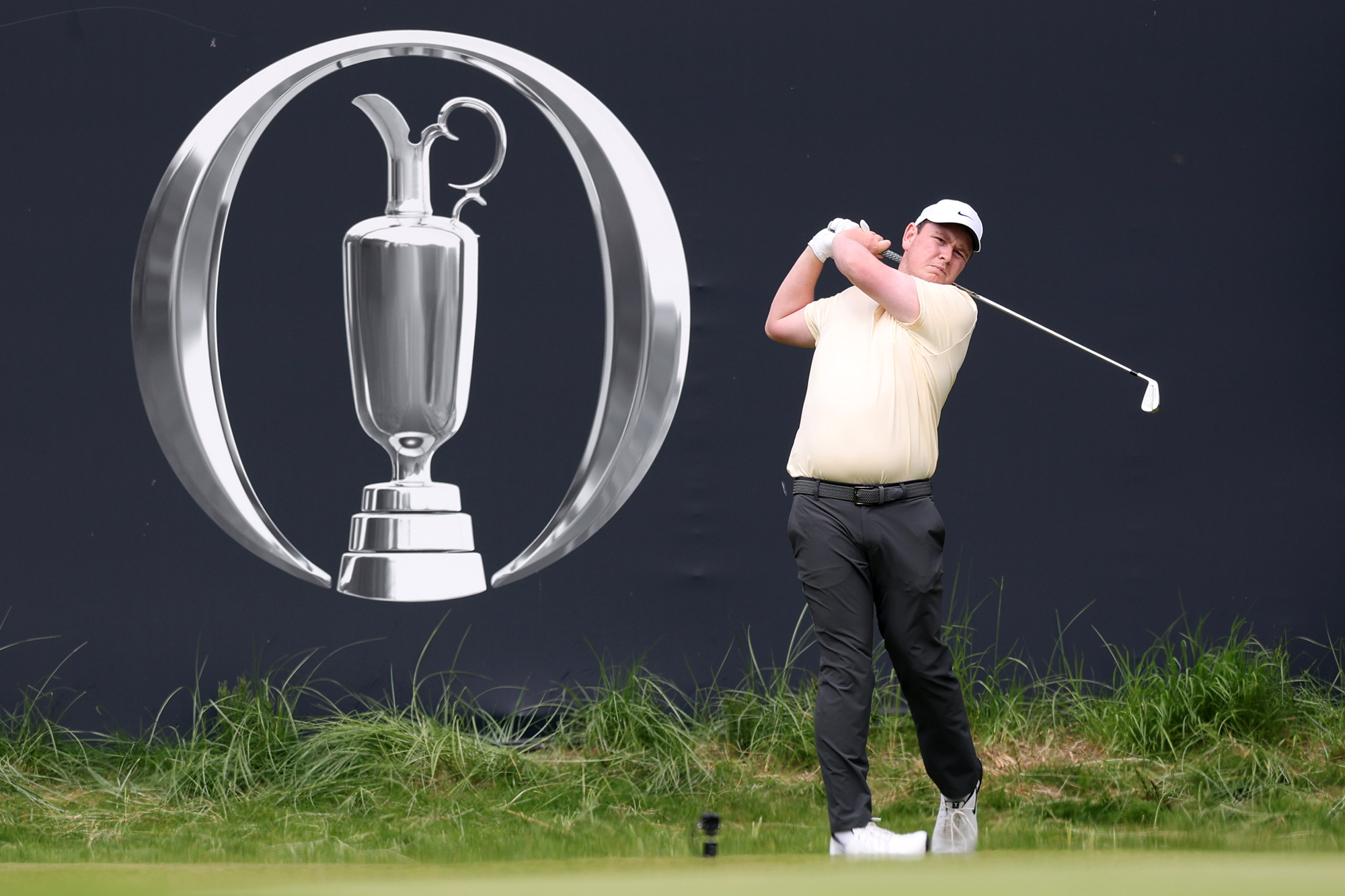 Robert MacIntyre hitting a tee shot in a practice round for the Open Championship at Royal Portrush in front of a huge logo for The Open