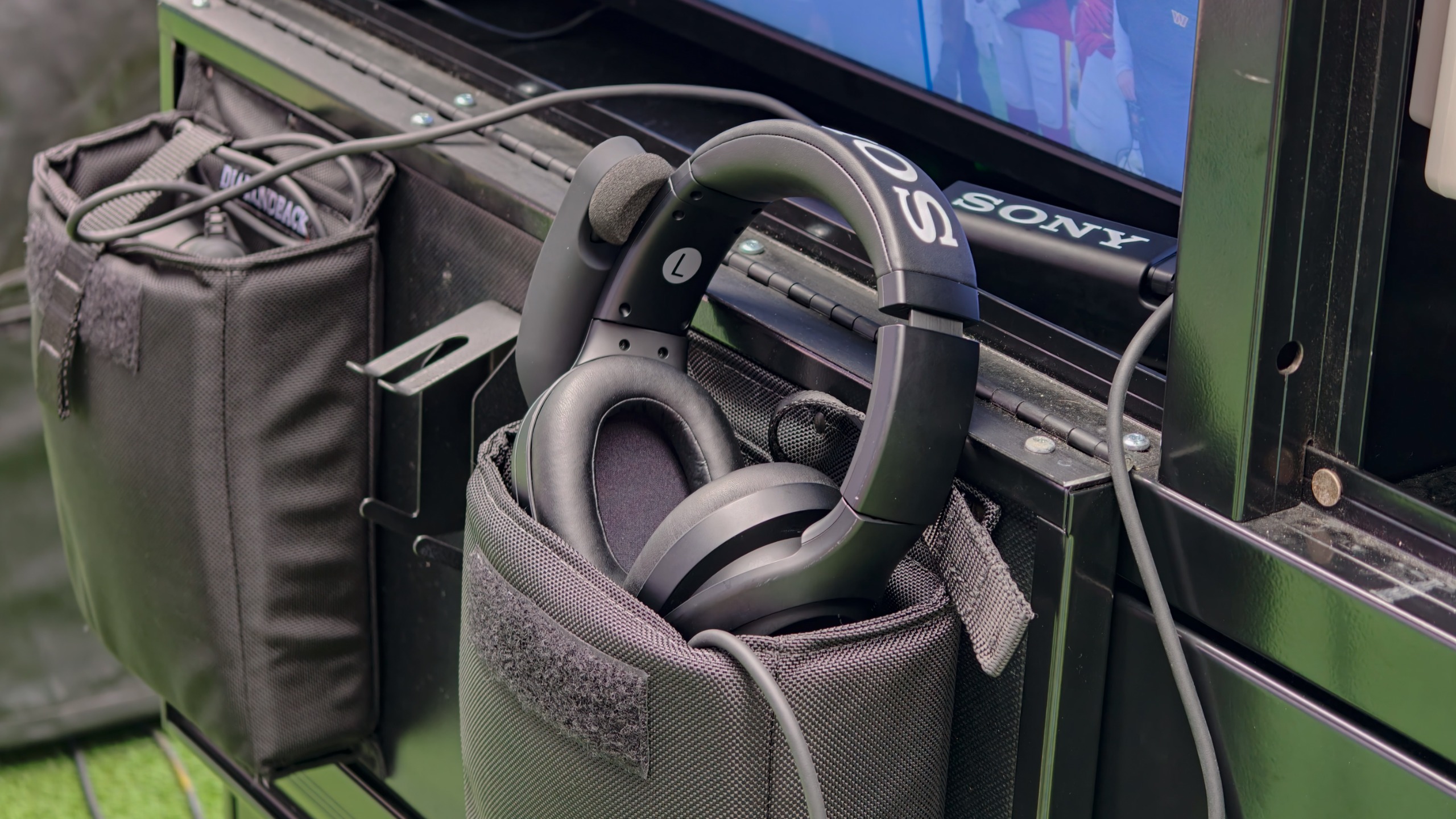 Sony broadcast headset resting in a padded equipment pouch beside a monitor and other sideline technology.