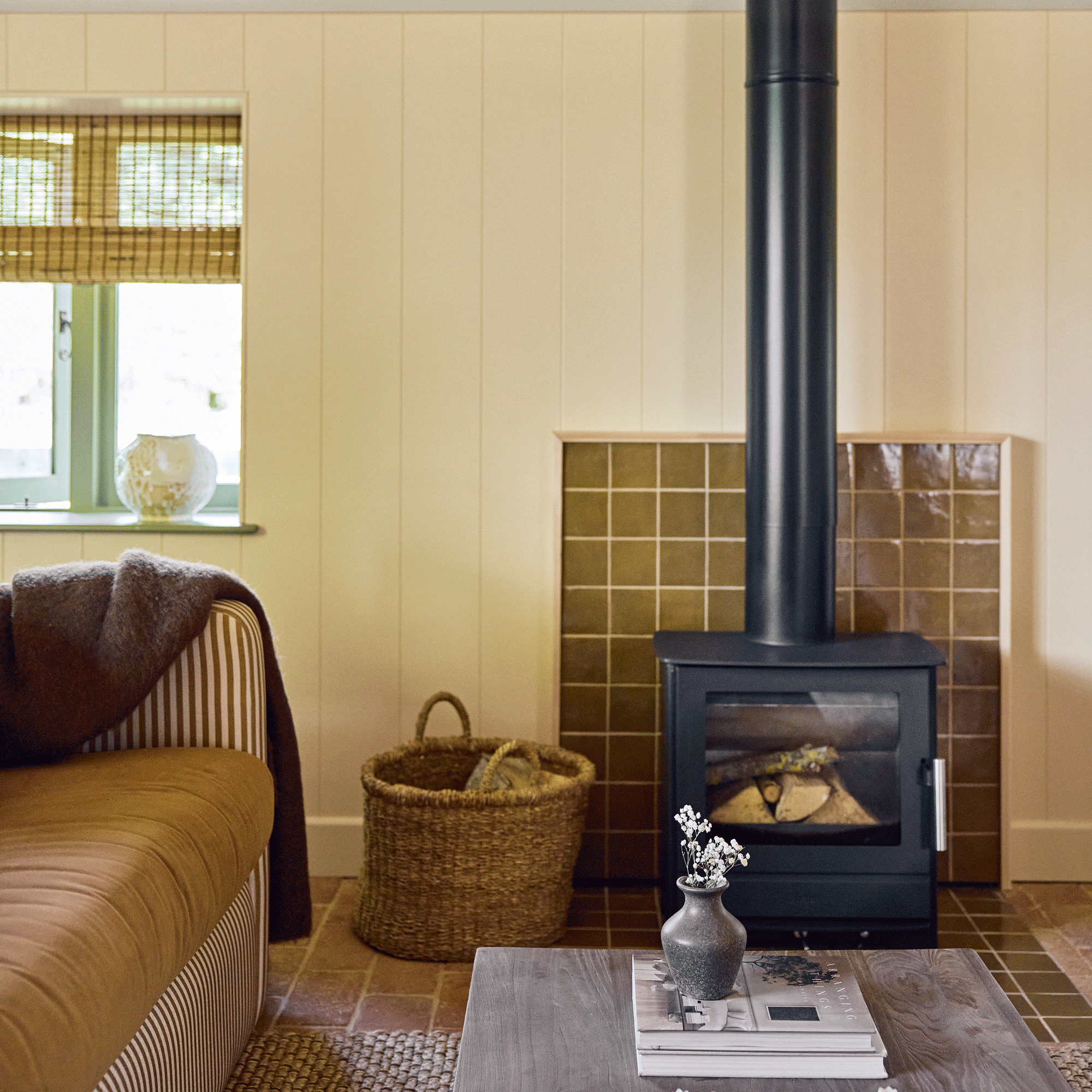 a pale yellow living room with a log burner and a square brown tiled hearth