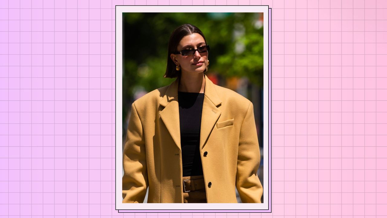 Hailey Bieber pictured walking down the street in NYC, wearing an oversized camel coat and sunglasses - used for a piece on Hailey Bieber&#039;s perfume/ in a purple and pink template