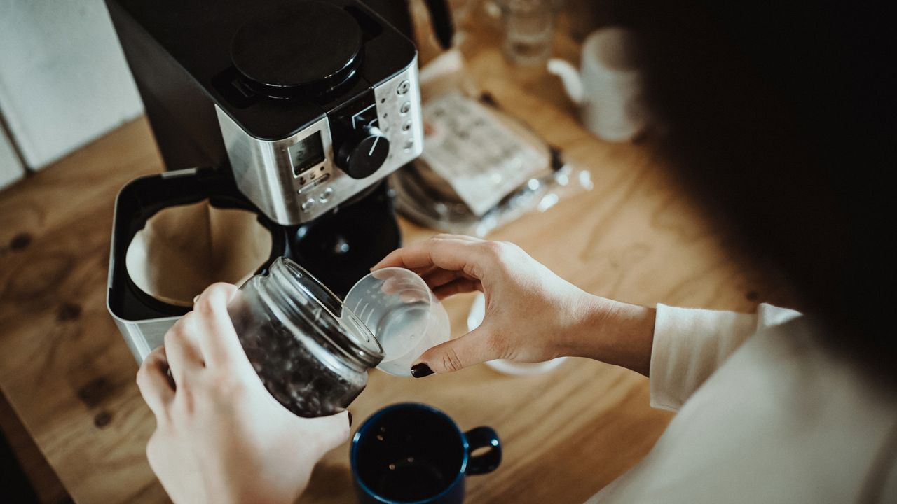 Person holding cup under coffee maker at home