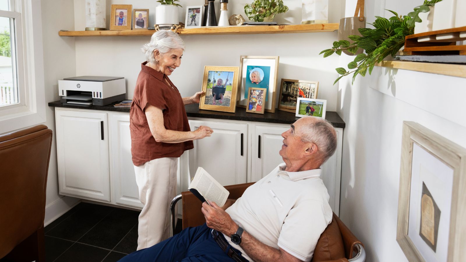 Grandparents smile at each other over a print of a baby picture with an HP smart tank printer in the background.