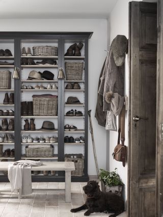 Black in-built shelving and hooks for shoes and hats in a boot room with a black dog