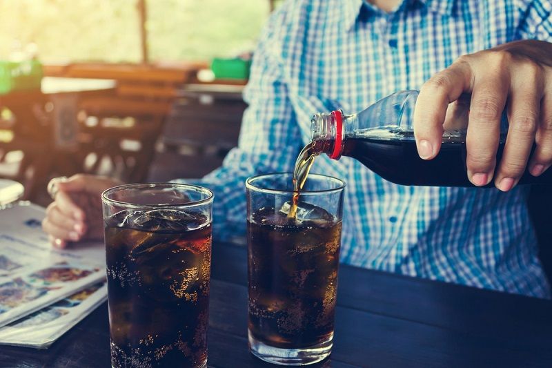 A person pouring soda into glasses.