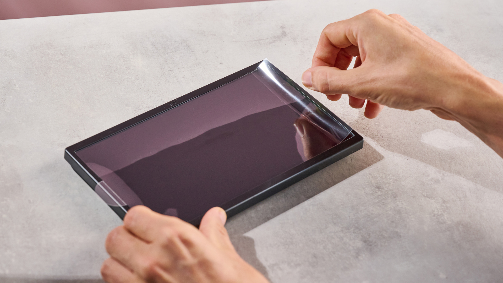 A man lining up and applying the Belkin Tempered Glass Anti-Reflective Screen Protector to the Nintendo Switch 2 using the supplied frame as a guide.