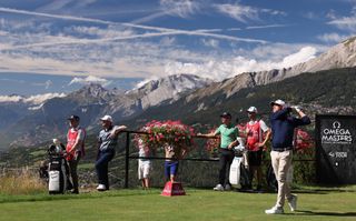 A golfer tees off with the Swiss Alps behind him