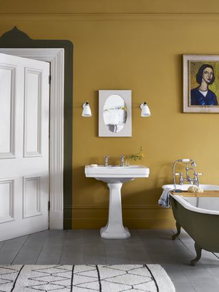 yellow bathroom with roll top bath, artwork, wooden floorboards, wall lights, rug