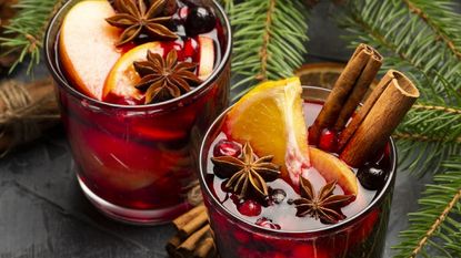 Two glasses of holiday cocktails with cinnamon, orange, and star anise