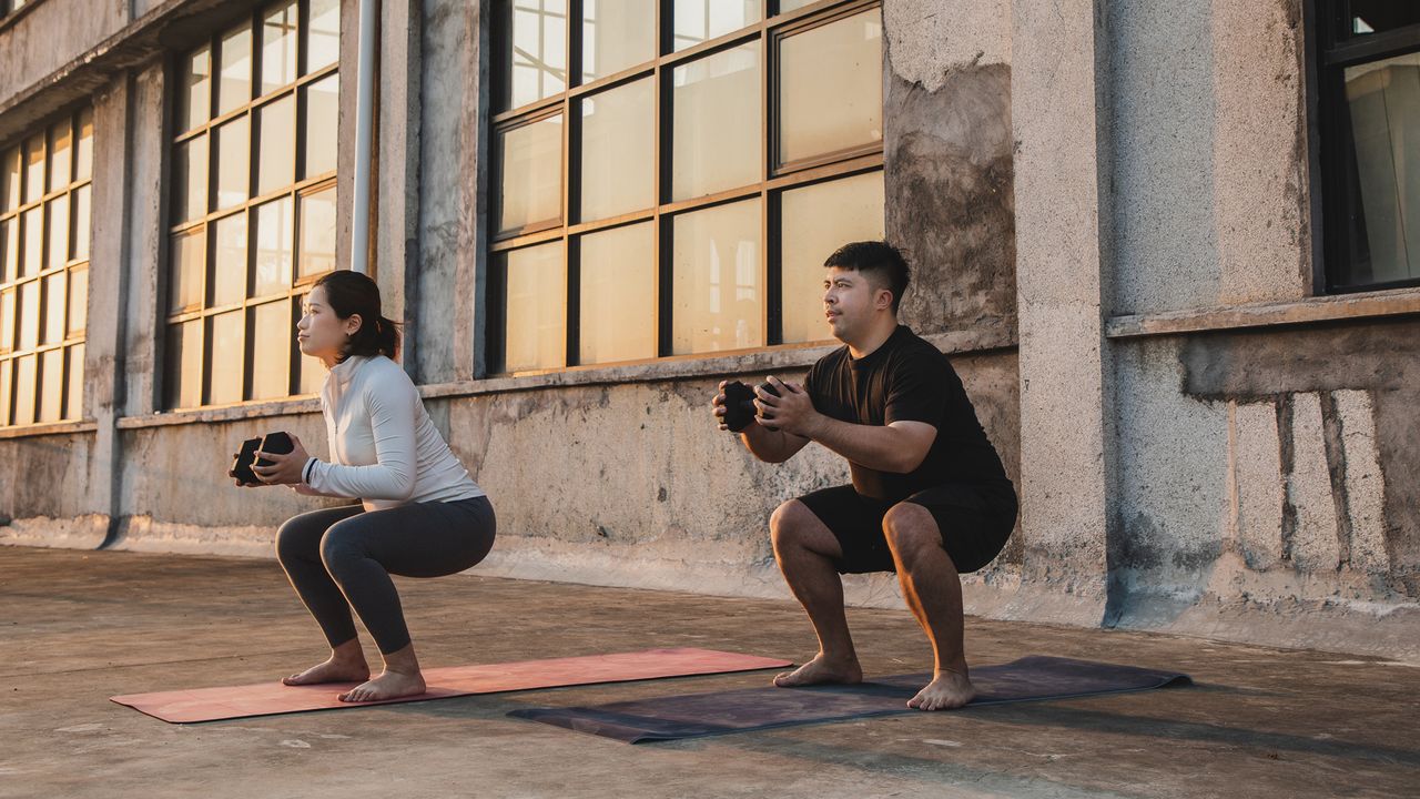 A man and woman perform a dumbbell workout together on mats