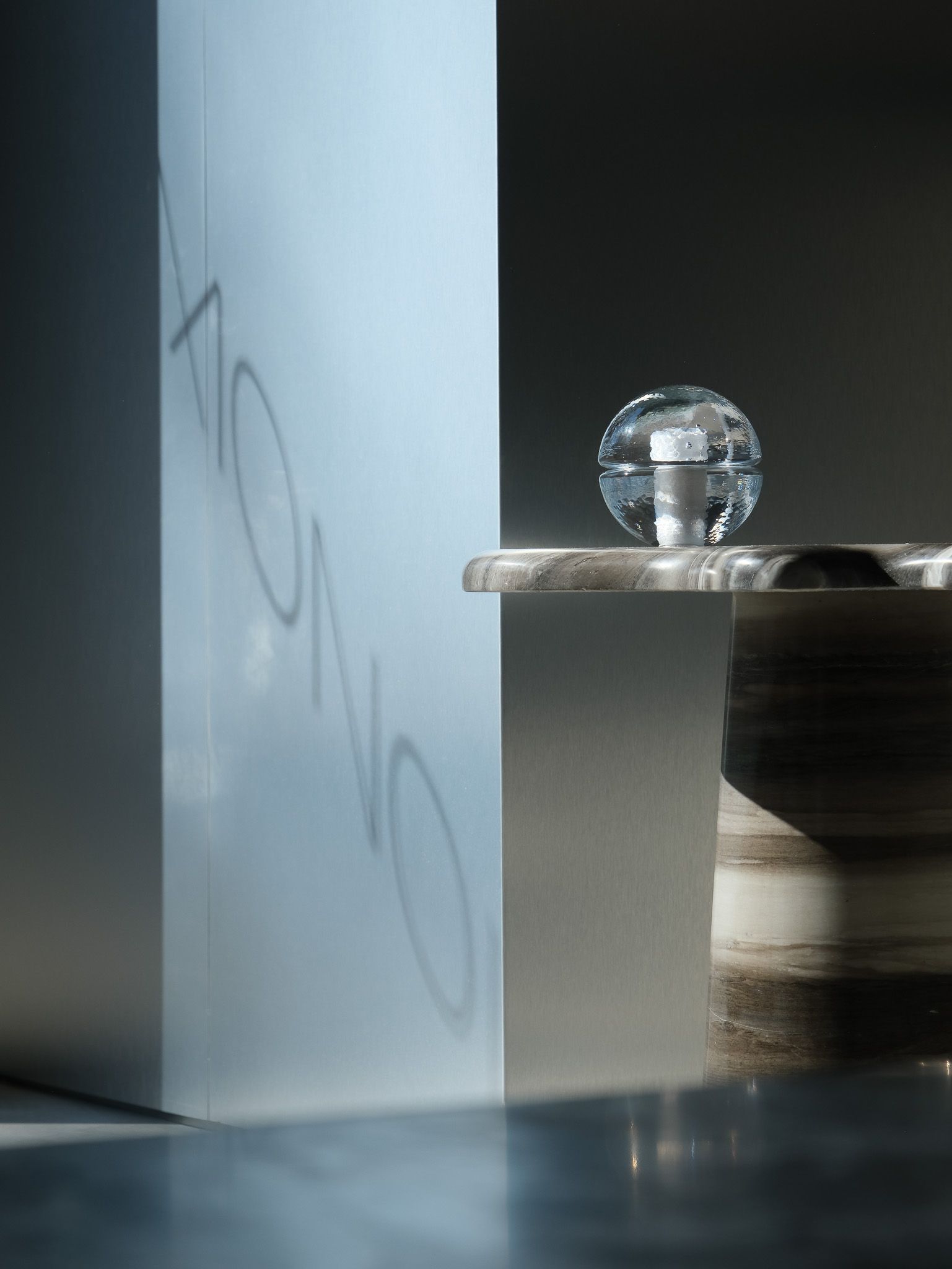 The interior of a brutalist, minial design showroom, decorated with contrasting furniture, artworks, and accessories in wood, earthy fabrics, reflective surfaces, and plants.
