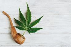 marijuana leaf coming out of wooden smoke pipe on whitewashed background