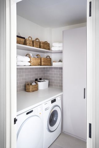 Small utility room ideas showing a floor to ceiling cupboard perpendicular to the washing appliances