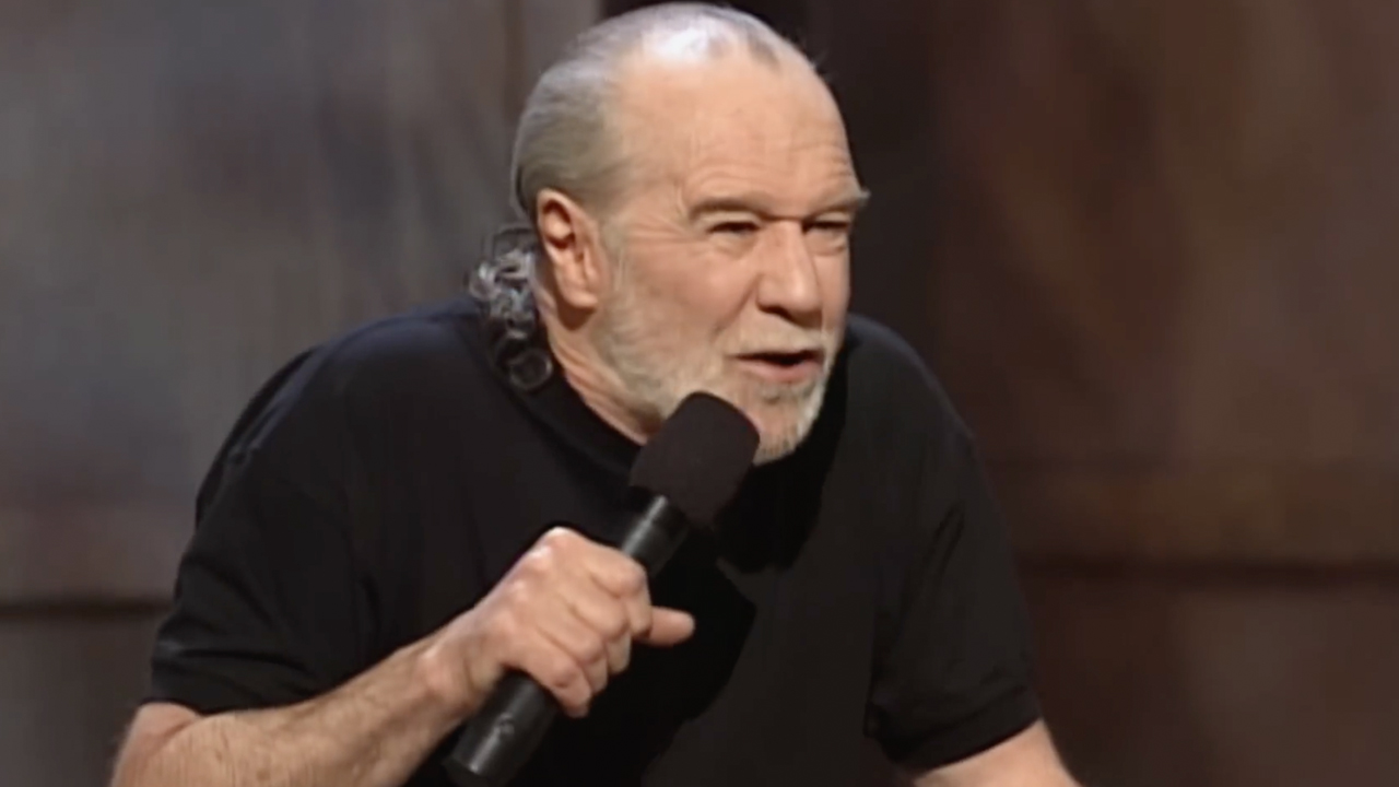 George Carlin, little older, performing stand up in his black shirt, footage from HBO's doc George Carlin's American Dream.