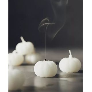 White Pumpkin Shaped Wax Candles, three are stacked in background in soft focus like a tiny pyramid and two are in focus up front with one wick just having been blown out and showing a plume of gray smoke rising up