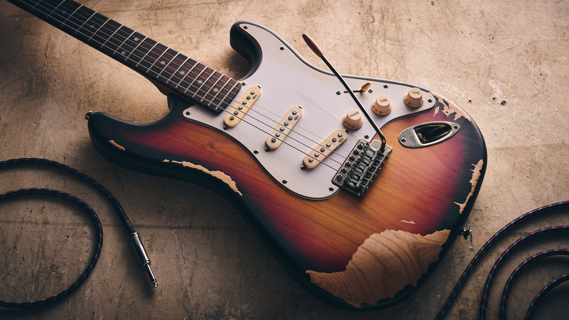 A Harley Benton ST-62HA electric guitar on a concrete floor with a guitar cable