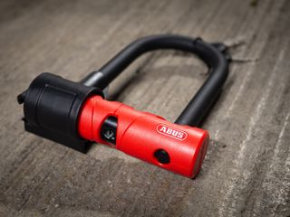 A black and red Abus Ultimate 420 lock and cable on a stone floor next to a bike rack